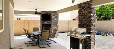 An outdoor patio with a stone fireplace, a grill, and a ceiling fan.