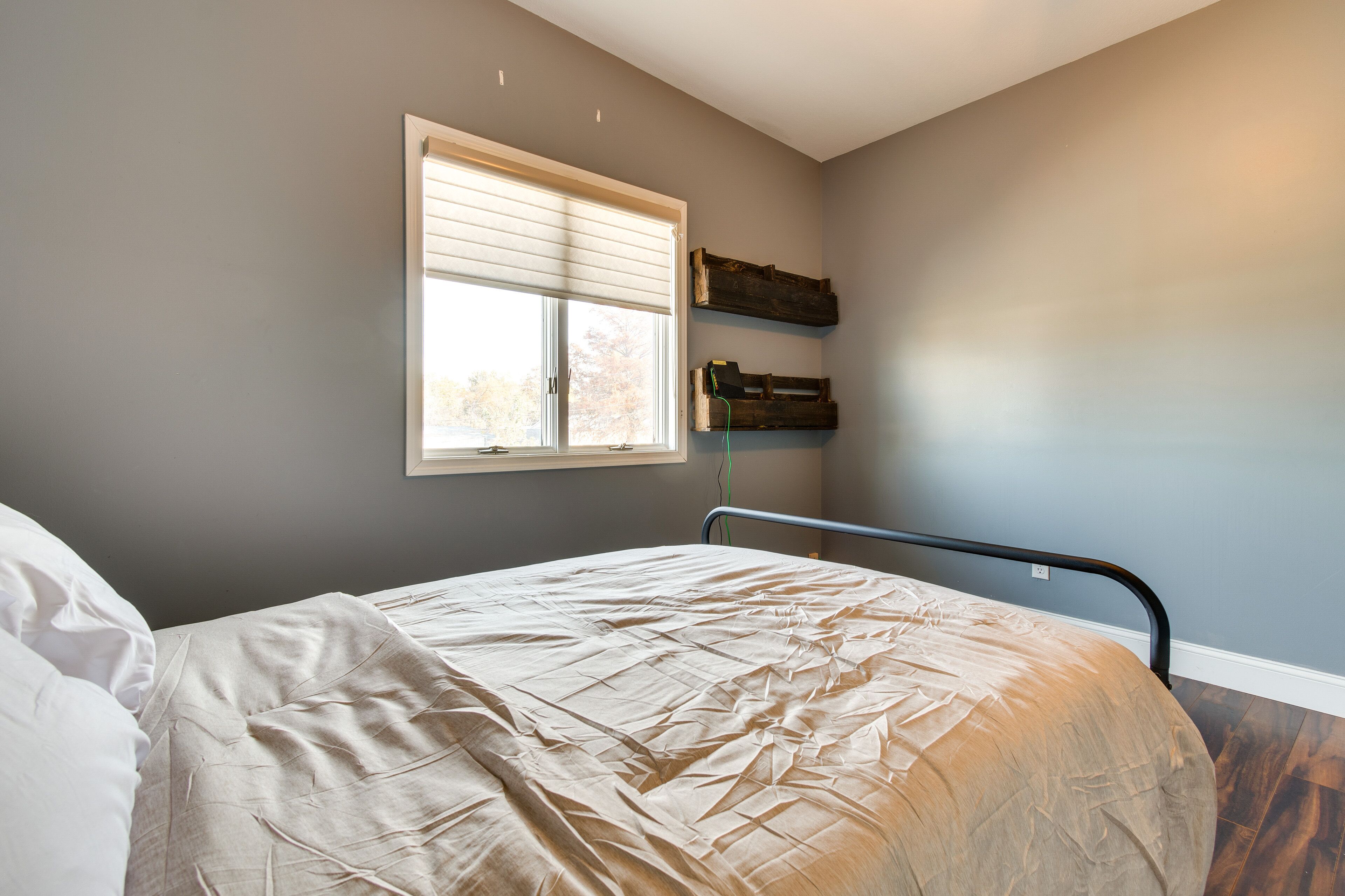 Un dormitorio con cama, una ventana con persianas y estanterías de madera en la pared.