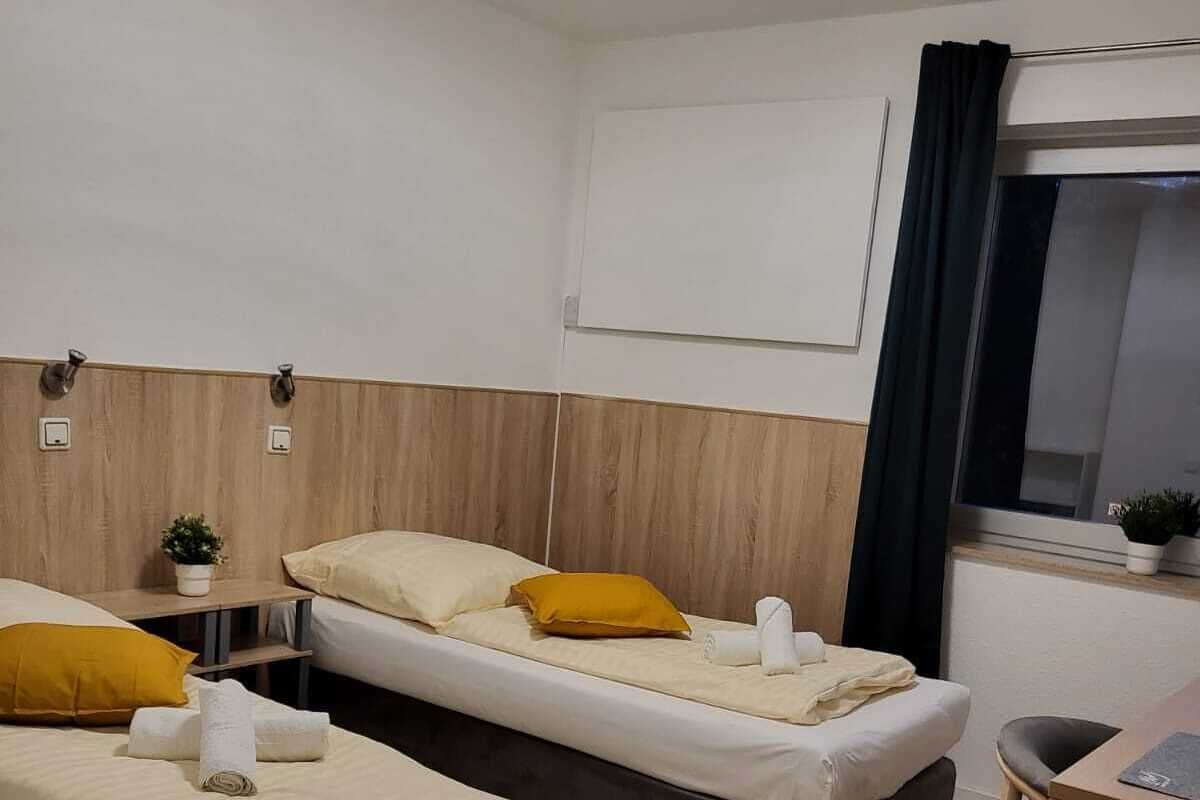 A hotel room with two beds, a small table, a window with curtains, and a desk.