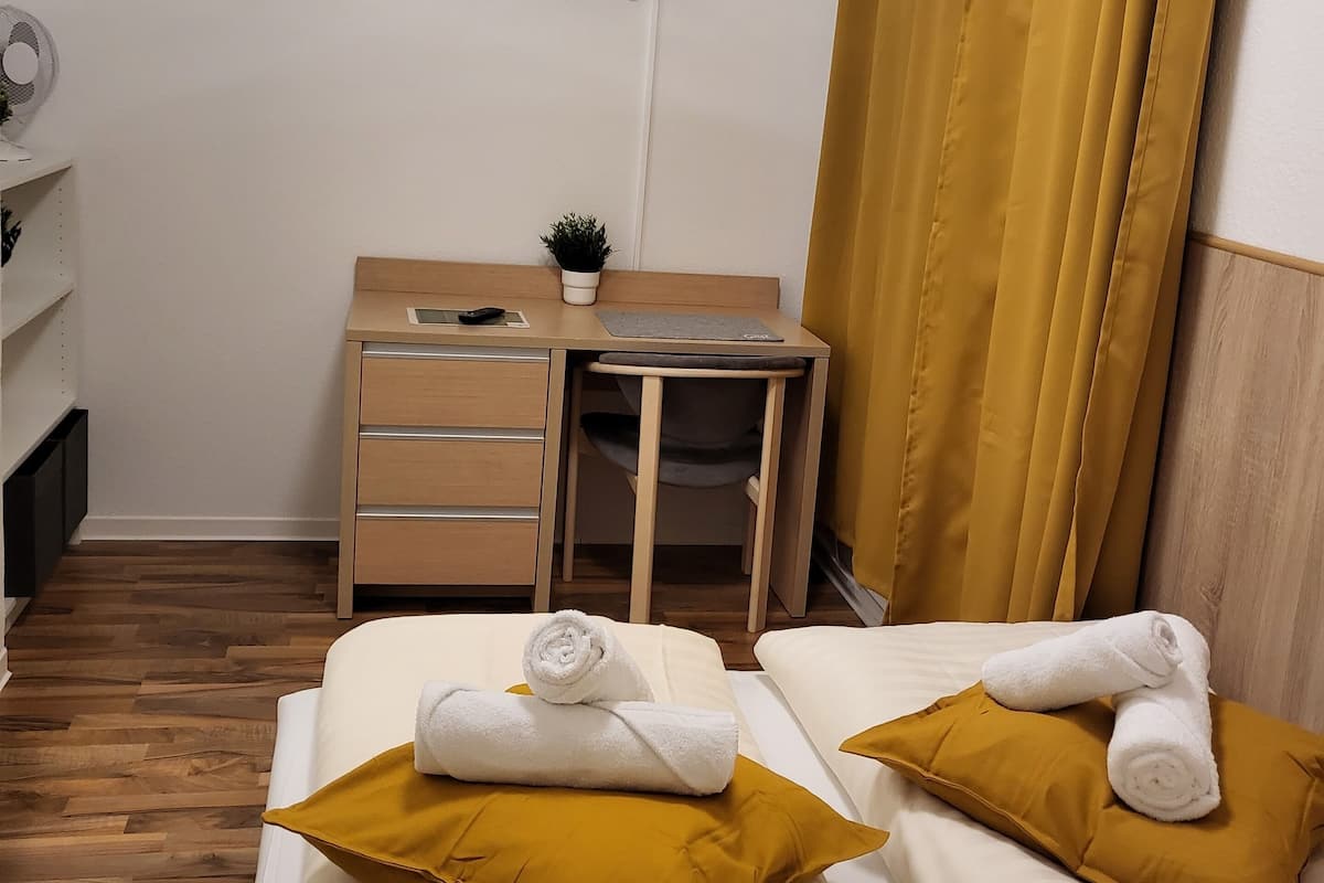 A hotel room with two beds, a desk with a chair, a TV mounted on the wall, and a window with curtains.