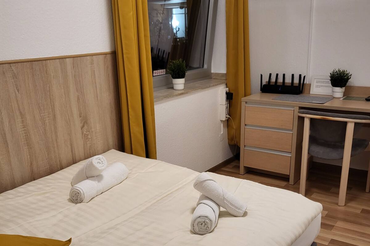 A hotel room with a bed, a desk, a chair, a TV, and a window with curtains.