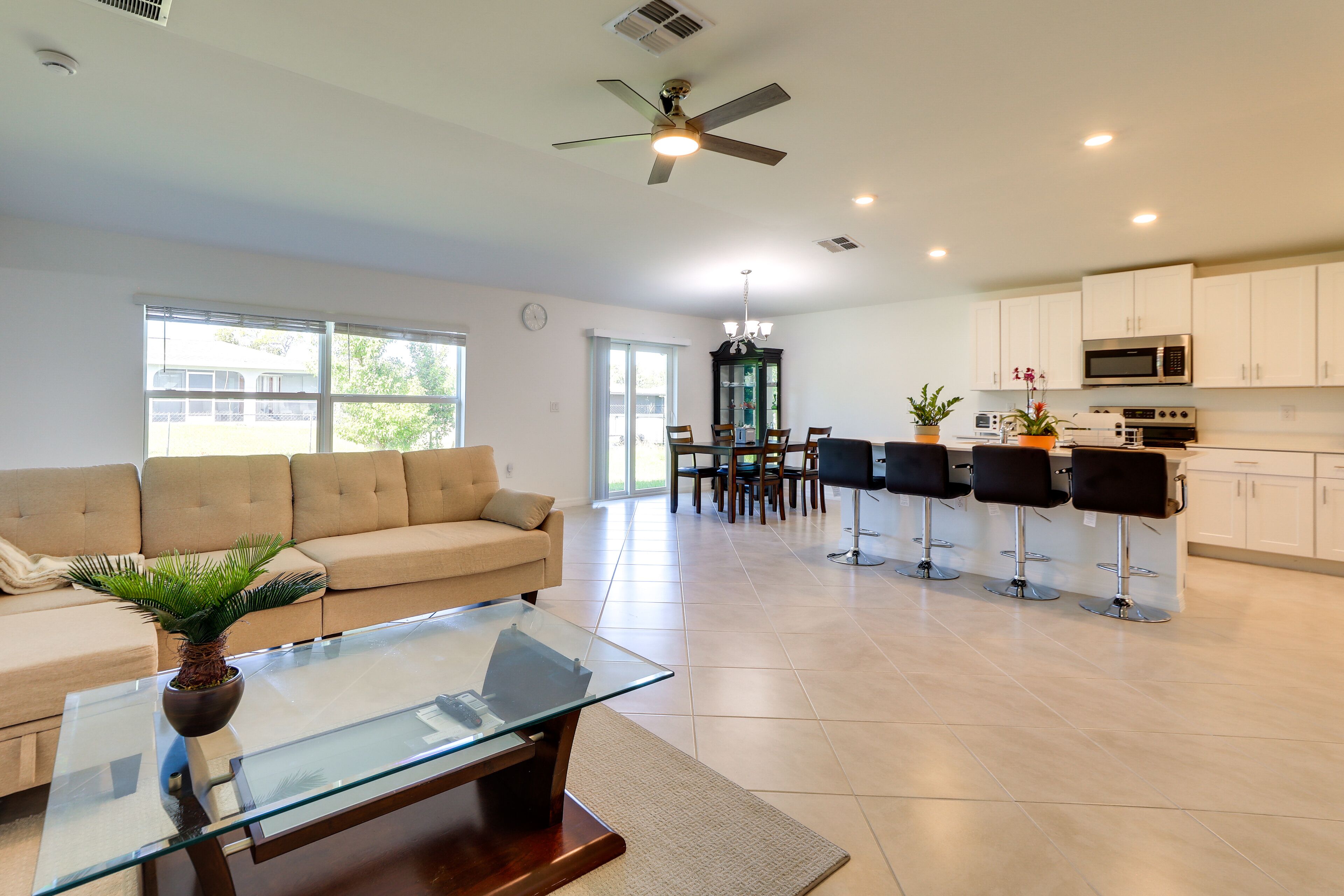 A modern living room with a glass coffee table, a beige sofa, and a dining area with a chandelier.