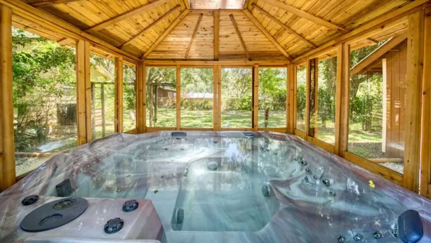 Una spa in legno con soffitto in vetro, vasca idromassaggio e vista sul verde circostante.