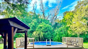 Un giardino con piscina, terrazza in legno e un gazebo.