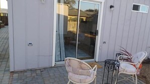 A building with a sliding glass door, two wicker chairs, and a small table on a paved patio.