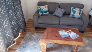 A grey sofa with patterned cushions, a wooden coffee table with magazines, and a grey patterned rug.