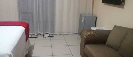 Habitación de hotel con cama, sofá, televisión montada en la pared y un pequeño calentador.