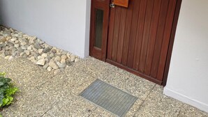 Une porte en bois avec un panneau de verre, une fenêtre à cadre blanc et un chemin de pierre menant à la porte.