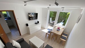 Un salon moderne comprenant un canapé, une table basse, un téléviseur fixé au mur et un coin repas avec une table et des chaises.