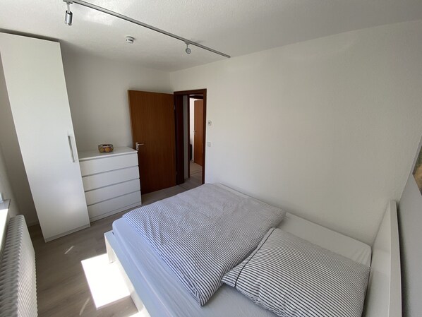 Un dormitorio con una cama, un aparador y una puerta que da a otra habitación.