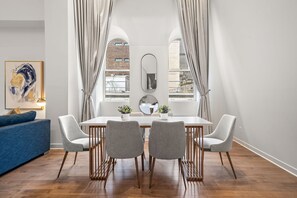 Uma sala de jantar moderna com uma mesa branca, cadeiras cinzas e um espelho grande acima.