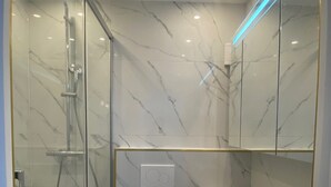 A modern bathroom with a glass-enclosed shower, a white toilet, and a marble backsplash.