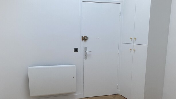 A room with a white door, a radiator, and wooden flooring.