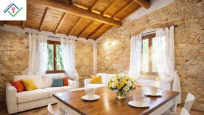 A cozy room with stone walls, wooden ceiling beams, white furniture, and a dining table with cups and a vase of flowers.