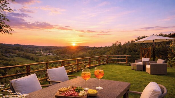An outdoor dining area with a table set for two, a wooden pergola, and a scenic view of a sunset over a hilly landscape.