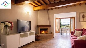 A living room with a fireplace, a television on a white cabinet, a red sofa, and a view of the outdoors.