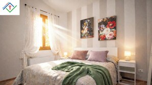 A bedroom with a bed, a nightstand, a window with curtains, and two floral paintings on the wall.