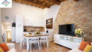 A modern kitchen with white cabinets, a wooden dining table, and a stone wall.