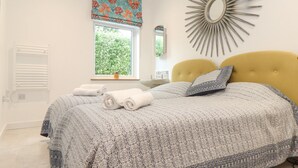 A bedroom with a bed, a window, a wall-mounted mirror, and a decorative sunburst mirror.