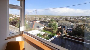 A room with a large window overlooking a residential area, a wooden bench, and a small plant.