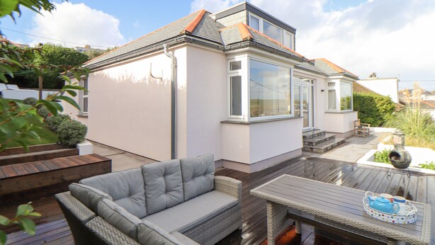A modern house with a covered patio, a glass conservatory, and a wooden deck.