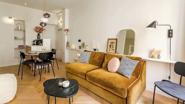 A modern living room with a mustard-colored sofa, black and white striped pillows, a black coffee table, and a white pendant light.