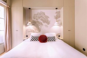 Quarto com cama, duas mesas de cabeceira, almofada vermelha e luminária fixada na parede.