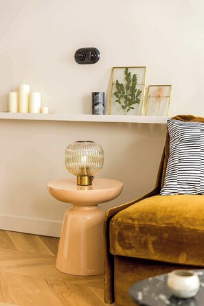 Uma sala de estar acolhedora com uma mesa redonda, um sofá e uma estante com velas e objetos decorativos.