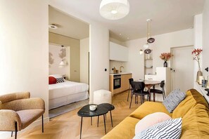 A modern, compact living space with a sofa, a dining table, a kitchen area, and a separate sleeping area.