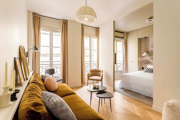 A modern hotel room with a sofa, a small round table, a bed, and a balcony with curtains.