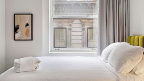 A hotel room with a neatly made bed, a window with a view of classical architecture, and a framed abstract painting on the wall. - Nomade MTL, Old MTL, Luxury 2BD 2BA, St Jacques (Montréal)