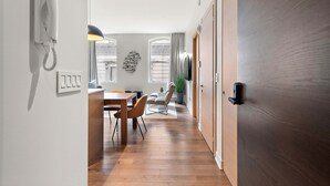 A modern kitchen with a built-in phone, a dining area with a wooden table and chairs, and a view of the city through large windows. - Nomade MTL, Old MTL, Luxury 2BD 2BA, St Jacques (Montréal)