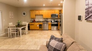 A compact kitchen with wooden cabinets, a microwave, a stove, and a dishwasher. There is a dining table with chairs and a couch in the living area. - Unit B (Moss Point)