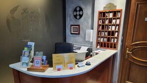 A hotel reception desk with a wooden counter, a clock, a key display, and informational brochures. - Hotel Ristorante delle Valli  (Germagnano)