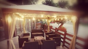 An outdoor seating area with cushioned chairs and tables, string lights, and a wooden fence. - Hotel Ristorante delle Valli  (Germagnano)