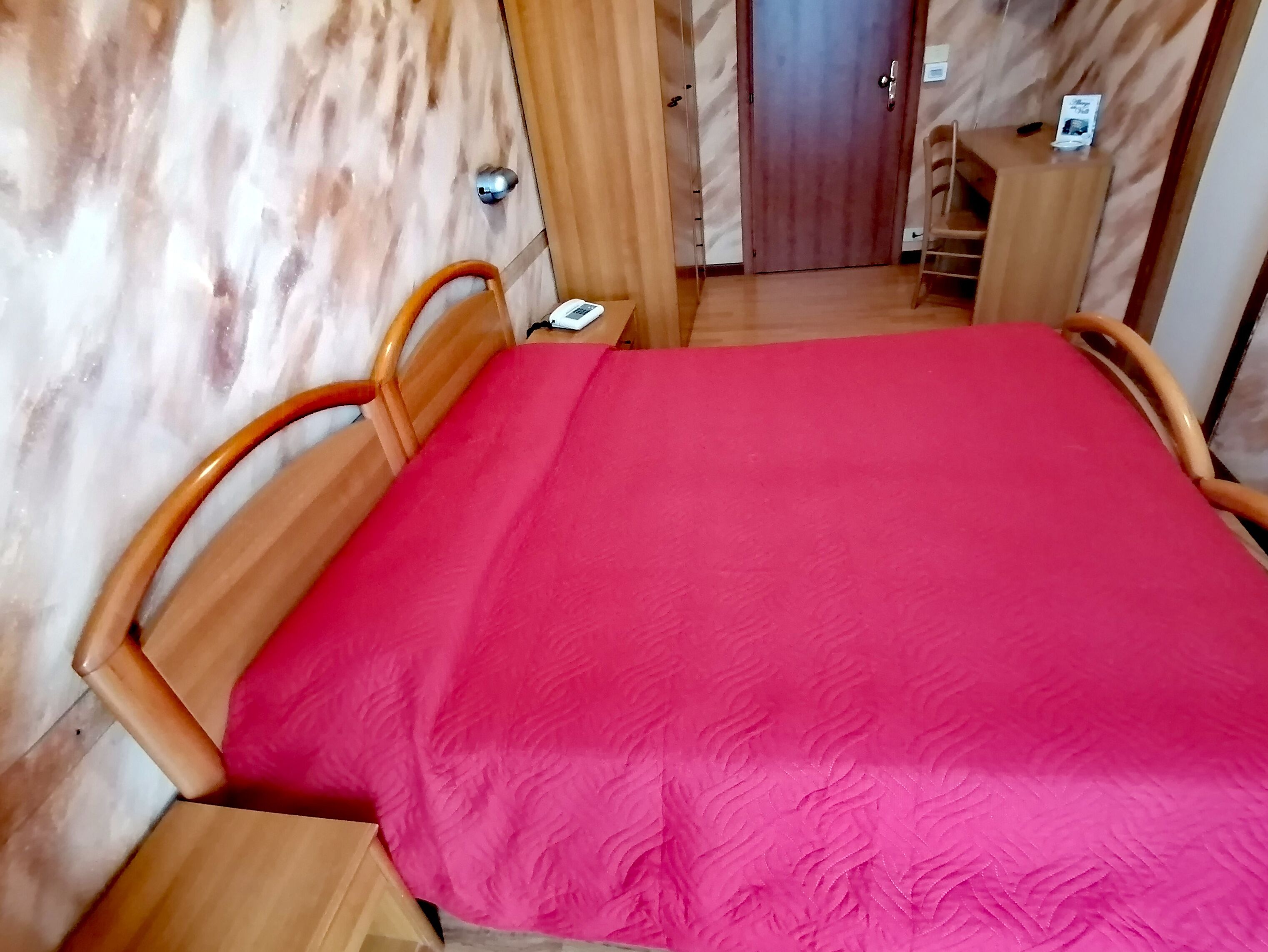Ein Zimmer mit einem Holzbett, einer roten Bettdecke und einem Schreibtisch mit Stuhl.