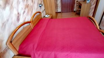 Ein Zimmer mit einem Holzbett, einer roten Bettdecke und einem Schreibtisch mit Stuhl.