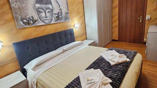 A bedroom with a bed, a headboard, a wardrobe, a door, and a wall with a painting. - Hotel Ristorante delle Valli  (Germagnano)
