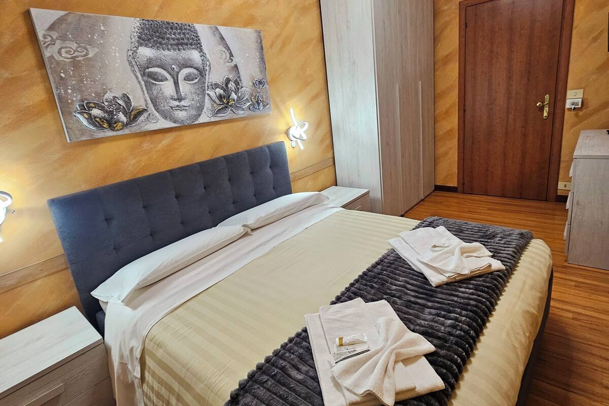 A bedroom with a bed, a headboard, a wardrobe, a door, and a wall with a painting.