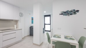A modern kitchen with white cabinets, a sink, and a clock on the wall. There is a dining area with a white table and green chairs, and a wall with a fish decoration. - Casa Arrullo Las Canteras - next to the beach (Las Palmas de Gran Canaria)