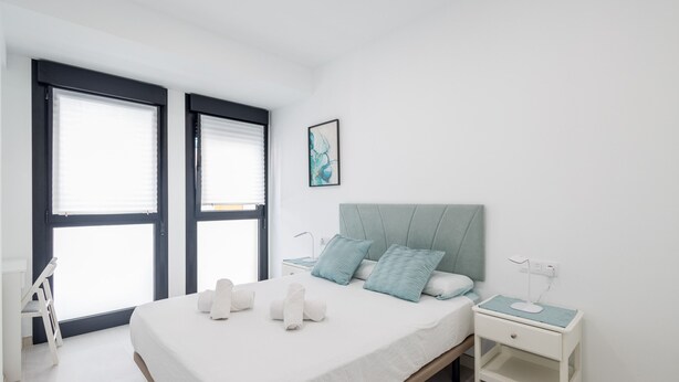 A bedroom with a bed, two bedside tables, a nightstand, and a window with blinds. - Casa Arrullo Las Canteras - next to the beach (Las Palmas de Gran Canaria)