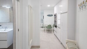 A modern kitchen with white cabinets, a dining area with a table and chairs, and a small bed with a striped pillow. - Casa Arrullo Las Canteras - next to the beach (Las Palmas de Gran Canaria)