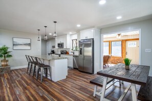 A modern kitchen with white cabinets, stainless steel appliances, and a wooden dining table. - Rustic Mountain Retreat: Cozy Sunroom, Pool, Theater & Hot Tub (Sevierville)