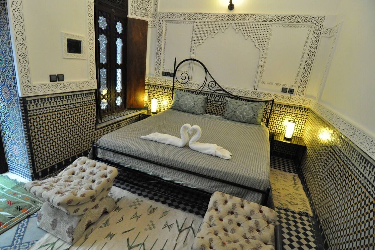 A bedroom with a bed, two nightstands, a decorative wall, and a patterned floor.