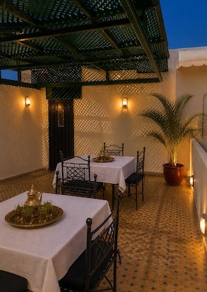 An outdoor dining area with tables and chairs, a potted plant, and a patterned floor. - Riad Youssef (Fes)
