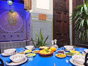 A dining table set with various dishes, surrounded by intricately patterned walls and a wooden door. - Riad Youssef (Fes)