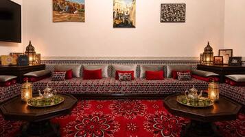 Um quarto com um sofá estampado, um tapete vermelho e duas mesinhas de cabeceira com bules e xícaras.