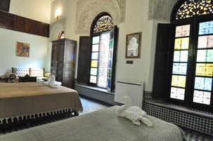 Quarto com duas camas, um armário de madeira, um quadro na parede e uma janela com vitrais.