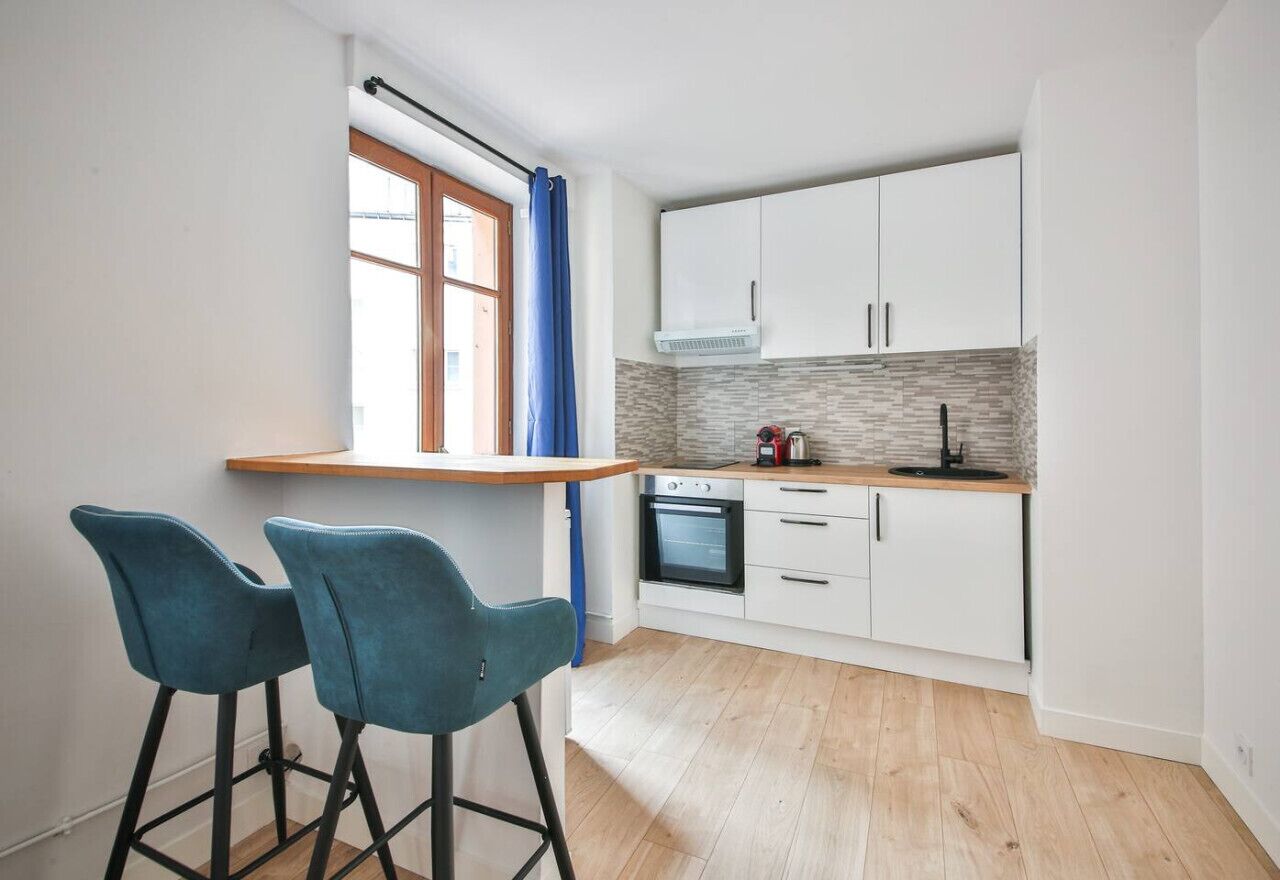Una cocina compacta con armarios blancos, horno integrado y ventana con cortinas azules.