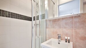 A modern bathroom with a glass shower enclosure, a white sink with two toiletries, and a tiled wall with a black and beige pattern. - 33.Studio 2Pers#Sèvres-Lecourbe#Champ-de-Mars (Paris)